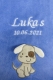 Copertina per neonati azzurro cielo, morbidissima, ricamata con il nome Lukas e la data di nascita 10/06/2021 in caratteri bianchi. Sotto, un cagnolino beige applicato con orecchie pendenti bianche e una macchia marrone. Simpatica e adatta ai bambini.